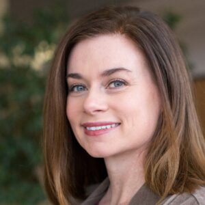 Rene Gutteridge is a white woman with shoulder-length straight brown hair. This is a headshot in front of a slightly blurred green background.